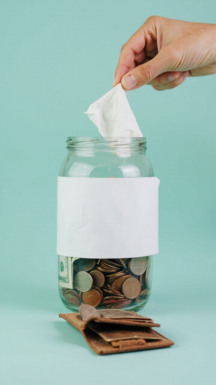 A Hand Placing Bill in Transparent Savings Jar